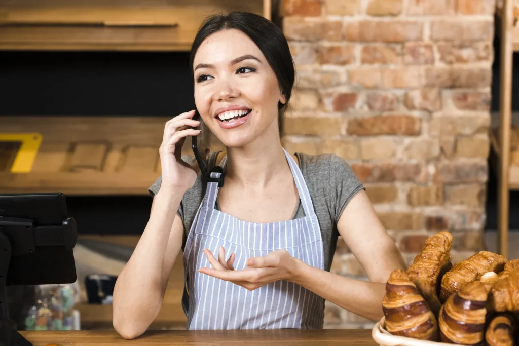 Titolare di una panetteria al bancone che parla al telefono sorridendo