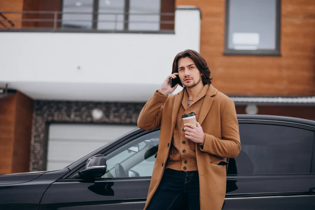 Uomo in cappotto al telefono con il cellulare accanto alla sua auto