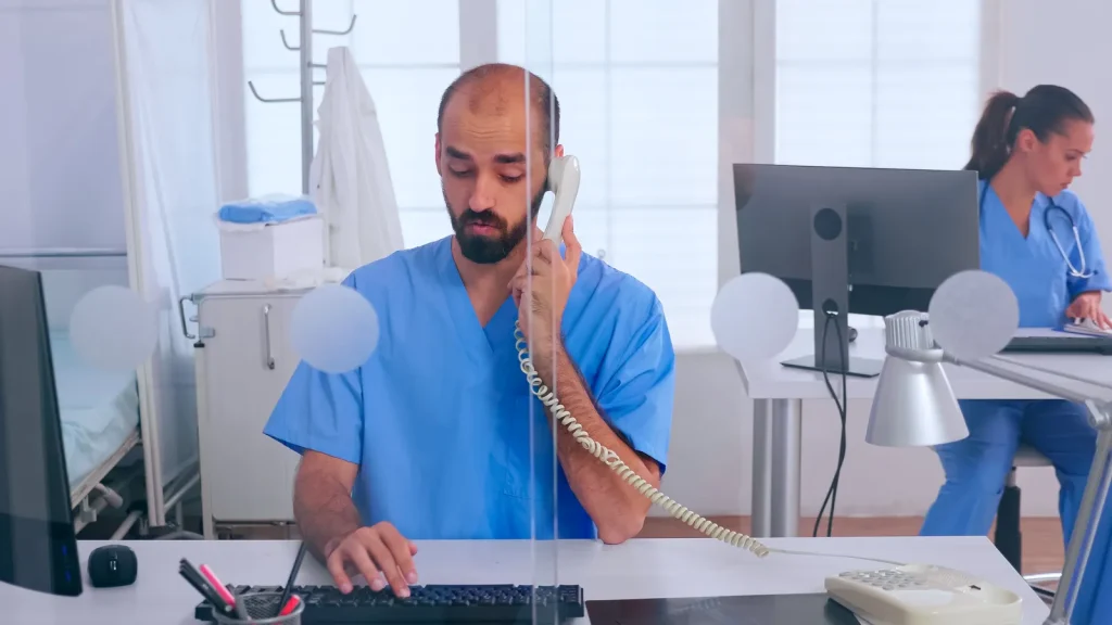 Segreteria di un poliambulatorio: un operatore sanitario al telefono e una collega al computer sullo sfondo
