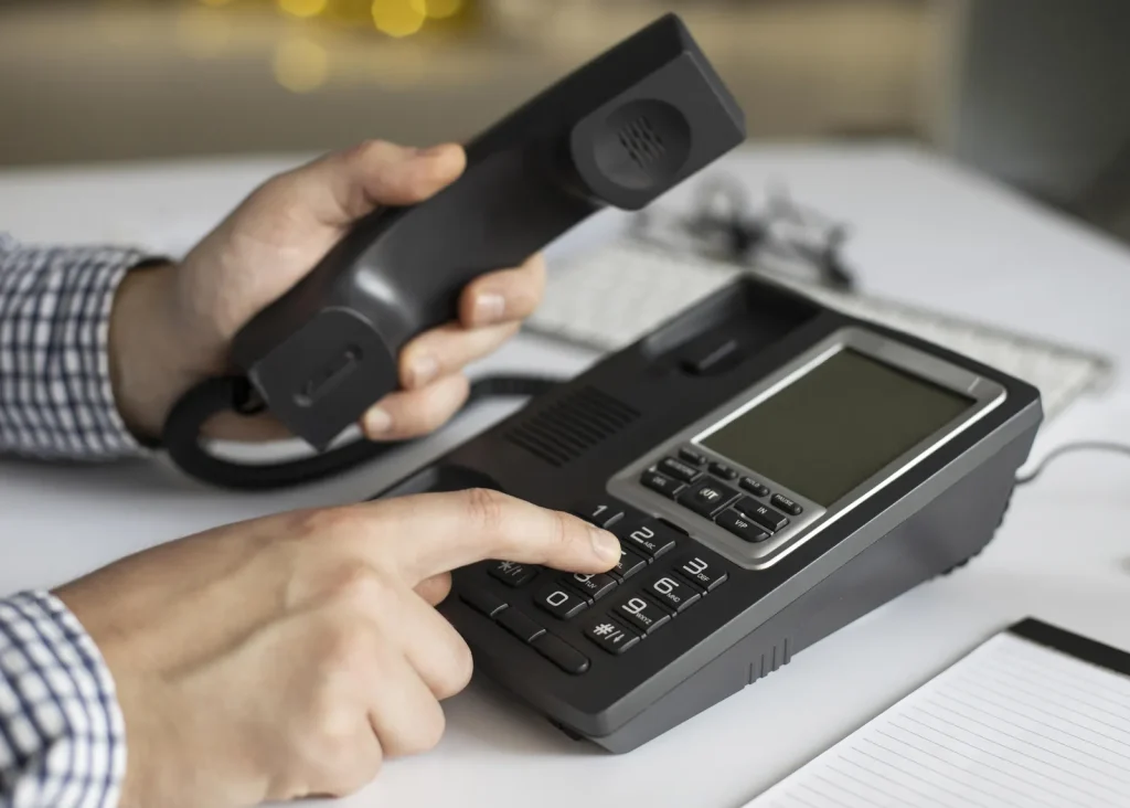 Mano che compone un numero sulla tastiera di un telefono da ufficio