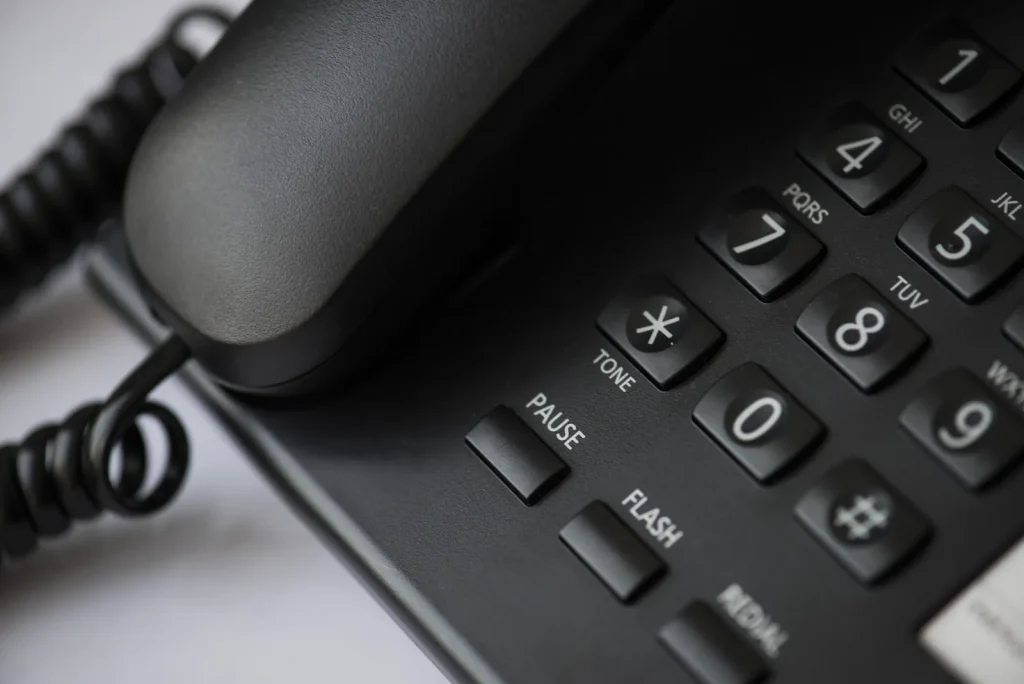 Mano che compone un numero sulla tastiera di un telefono da tavolo, in primo piano